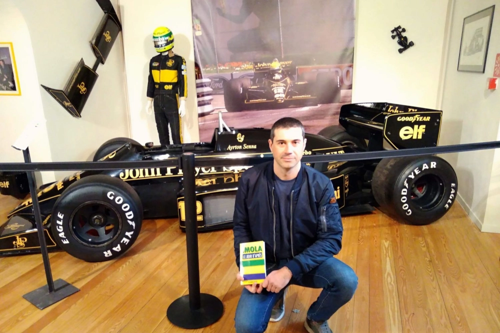 Ilario Pax posant avec son roman devant la Lotus-Renault d'Ayrton Senna